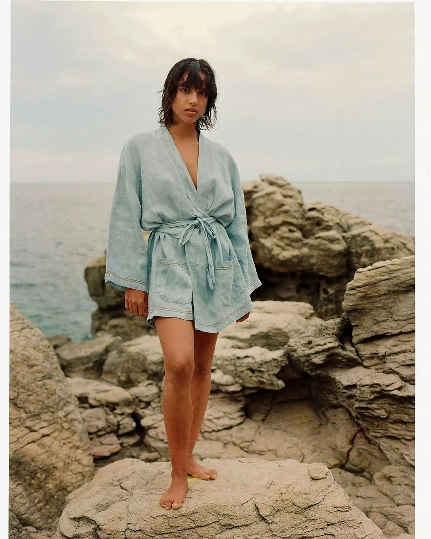 a woman in a blue robe standing on rocks near the ocean